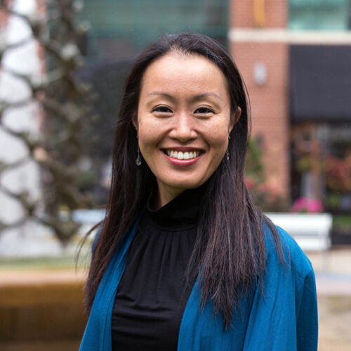 Image of a woman of east asian descent with long dark hair and a blue sweater smiling